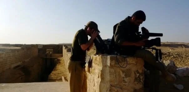 Two Chasing Mummies crew members working with a camera beside a stone wall in Egypt.