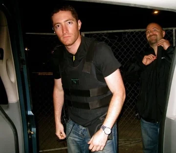 David Price wearing a protective vest beside a production vehicle while working on The Peacemaker